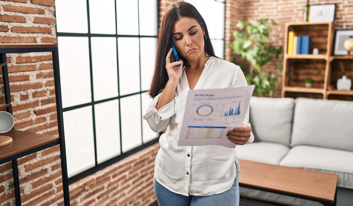 young hispanic woman speaking on the phone about bills depressed and worry for distress crying angry and afraid. sad expression
